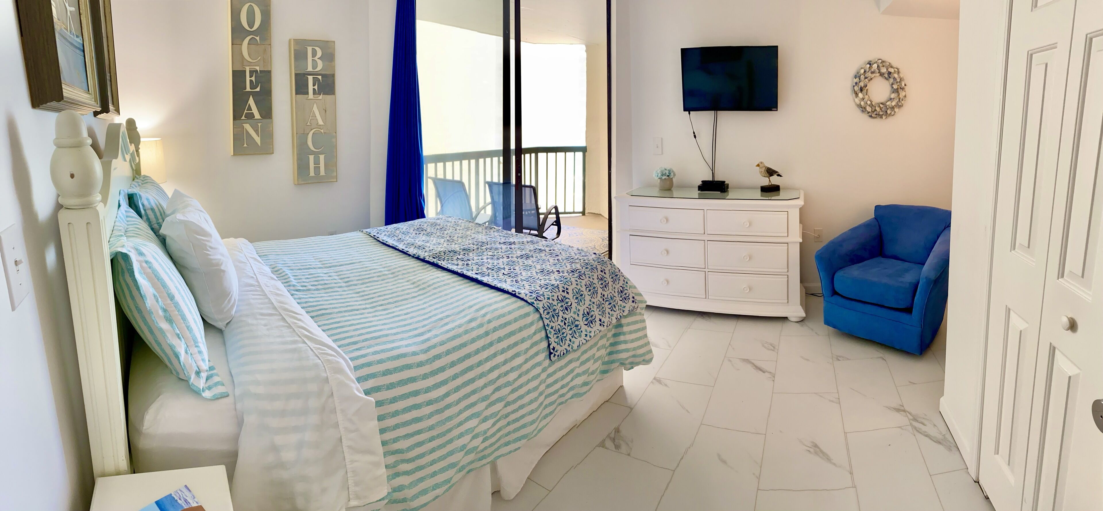 Ein Schlafzimmer mit Bett, Schminktisch, Stuhl, Fernseher und einem Balkon mit Aussicht.