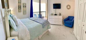 Un dormitorio con cama, cómoda, silla, televisor y balcón con vista.
