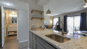 A modern kitchen with granite countertops, a stainless steel sink, and wooden shelves above the counter. - Bentley's Bungalow (Branson)