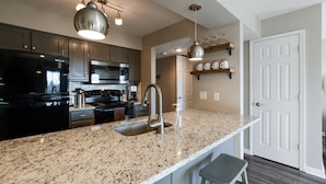 A modern kitchen with granite countertops, stainless steel appliances, and pendant lighting. - Bentley's Bungalow (Branson)