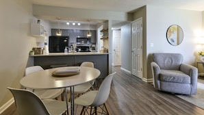A modern kitchen with a dining area, featuring a central island, pendant lighting, and a grey armchair. - Bentley's Bungalow (Branson)