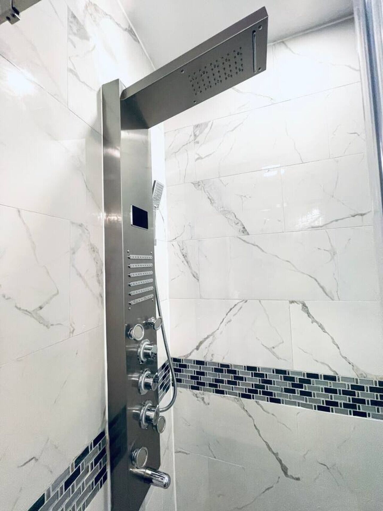 Une douche moderne dotée d’un pommeau de douche à pluie, de plusieurs robinets de contrôle et d’un mur carrelé au motif de marbre.