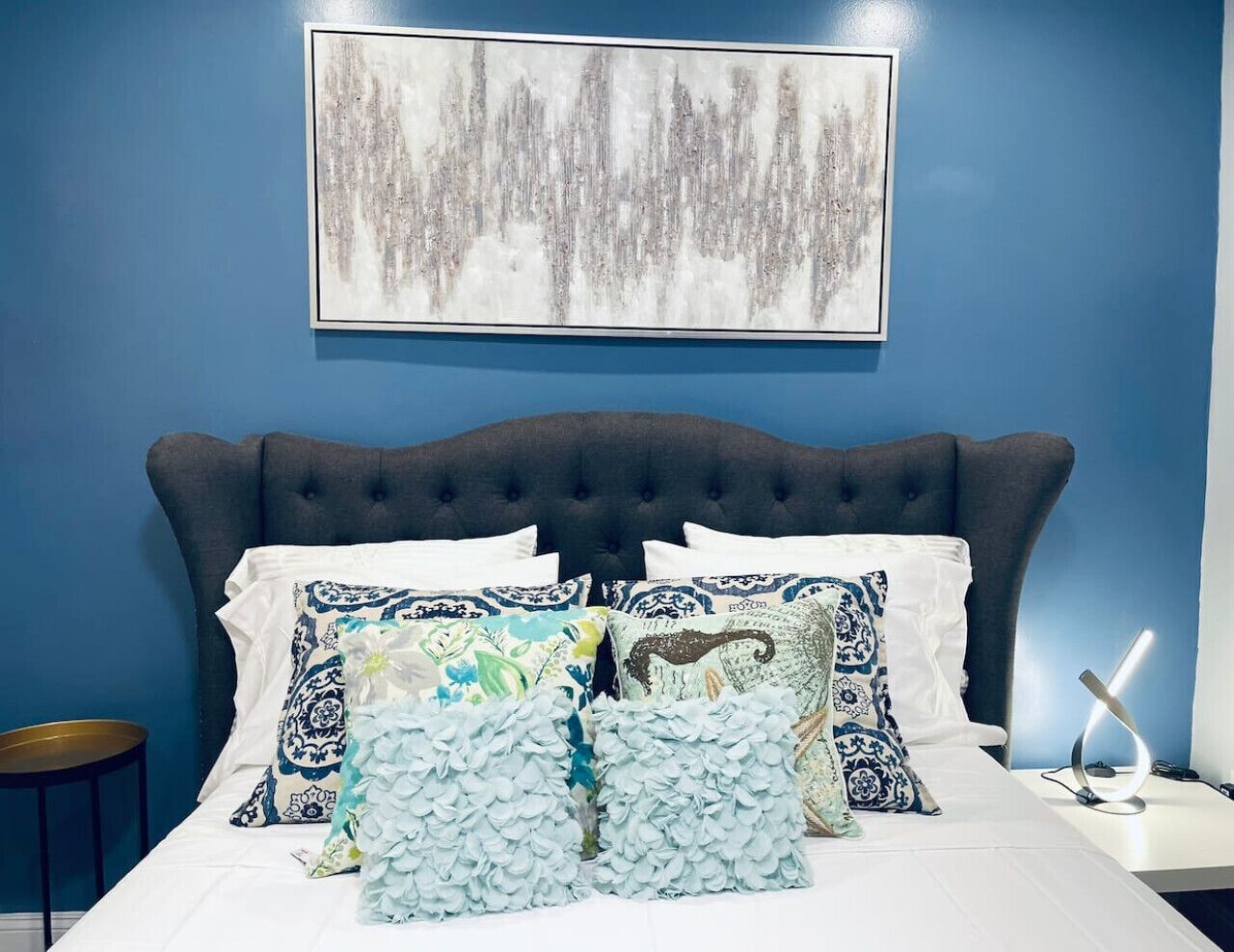 A bedroom with a dark headboard, white bedding, and multiple decorative pillows.
