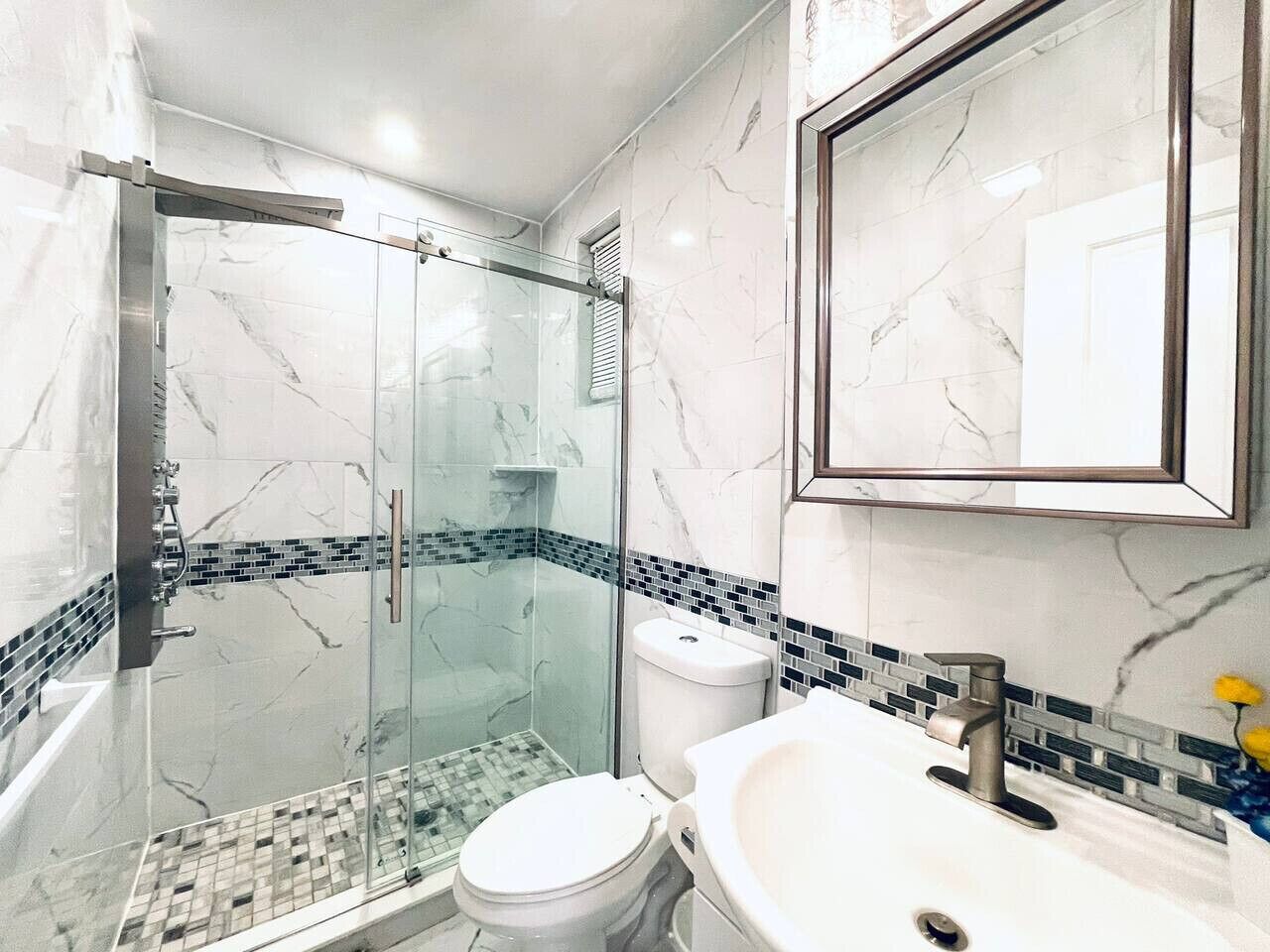 A modern bathroom with a glass-enclosed shower, a white toilet, and a sink with a marble countertop.