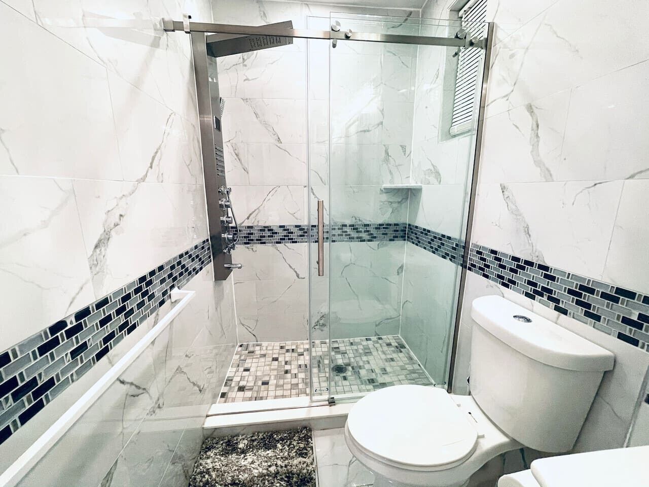 Une salle de bain moderne avec une douche à parois de verre, des toilettes blanches et un sol carrelé.