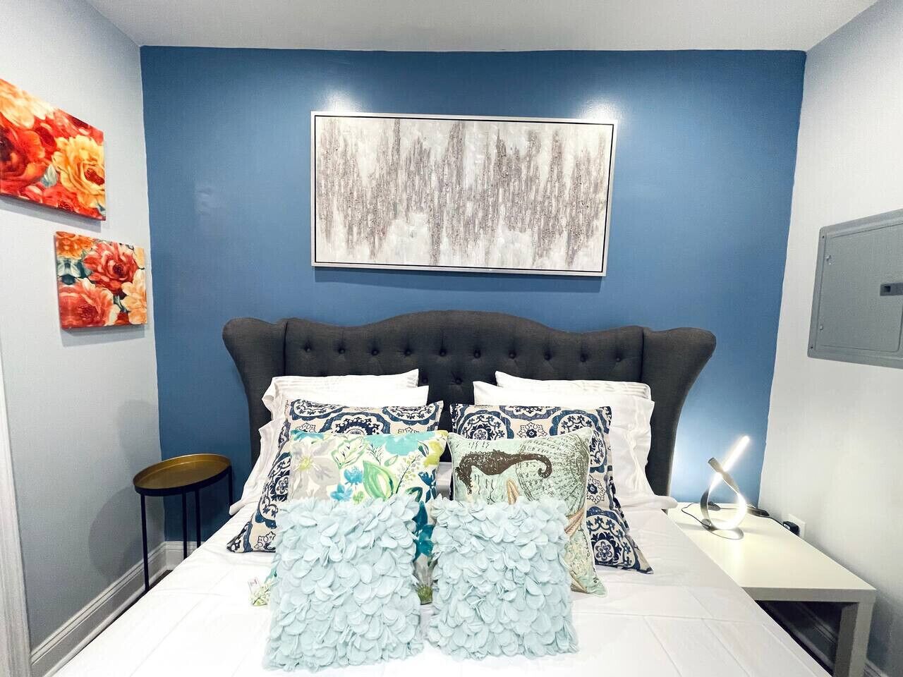 Quarto com cabeceira escura, roupa de cama branca e almofadas estampadas com motivos florais.