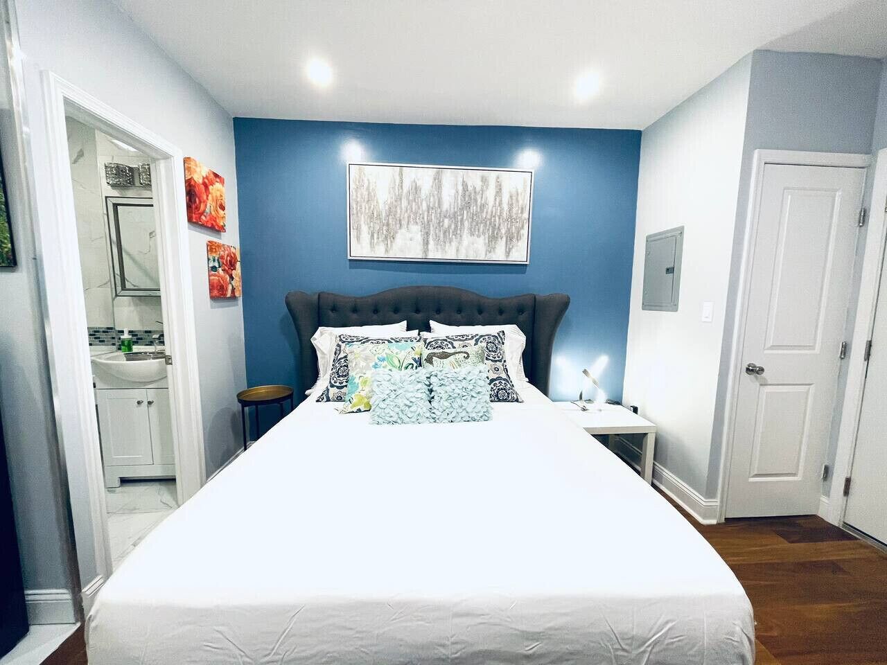 A bedroom with a large bed, a nightstand, a wall-mounted artwork, and a door.