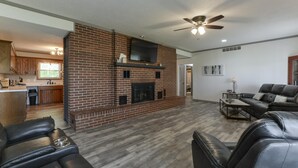 Ein geräumiges Wohnzimmer mit Kamin aus Backstein, Ledersofas und Deckenventilator.