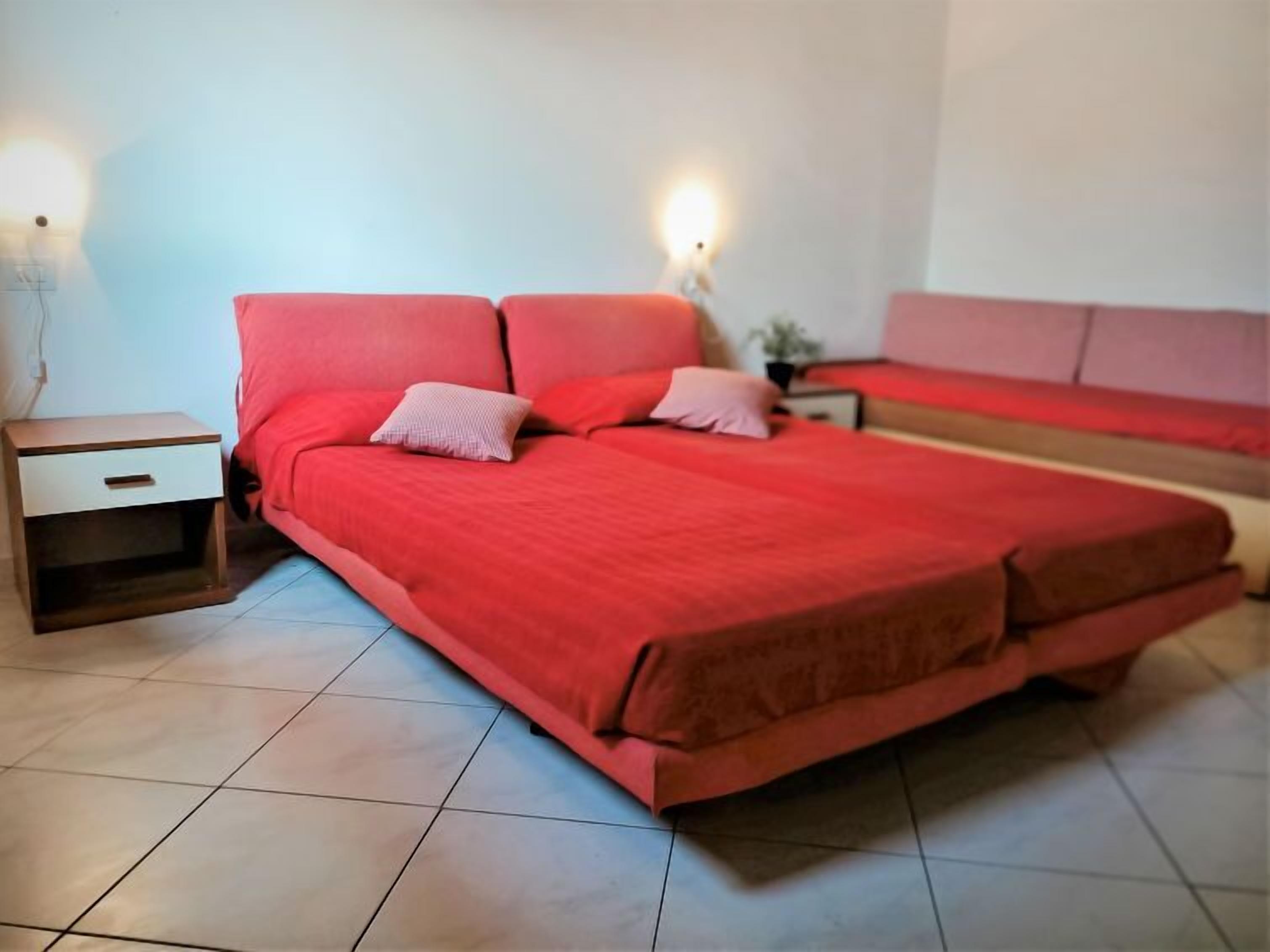 A bedroom with a large bed, a nightstand, and a wall-mounted lamp.