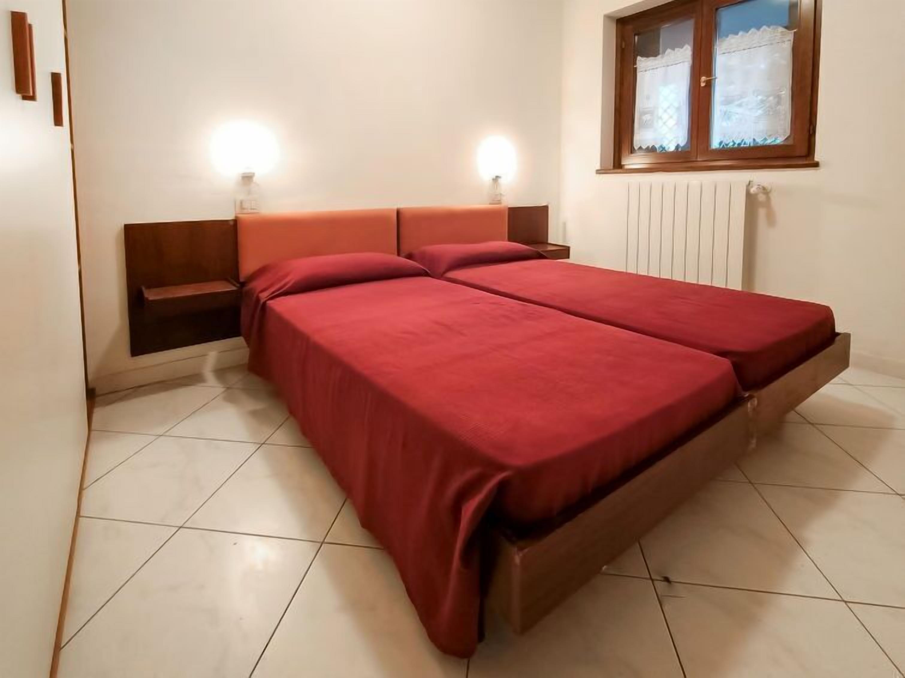 A double bed with a wooden headboard and two bedside tables, a window with a view, and a white radiator.