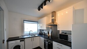 A modern kitchen with a washing machine, dishwasher, microwave, and stainless steel range hood.