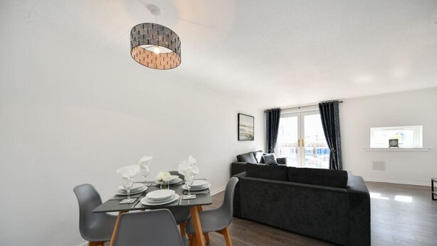 A modern living room with a grey sofa, a dining table set with plates and glasses, and a hanging light fixture.