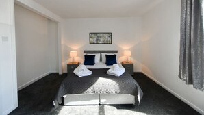 A hotel room with a bed, two bedside lamps, a painting on the wall, and a window with curtains.
