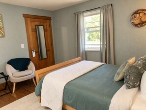 A bedroom with a bed, a chair, a window with curtains, a door, and a wall decoration.