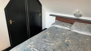 A bedroom with a bed, a nightstand, a wall-mounted light, and a black door. - Rain Hill Cottage - Sleeps 4, Parking & Pets Ok (Louth)