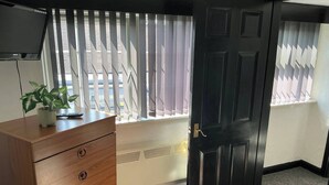 A room with a wooden dresser, a potted plant, a window with blinds, a black door, and a radiator. - Rain Hill Cottage - Sleeps 4, Parking & Pets Ok (Louth)
