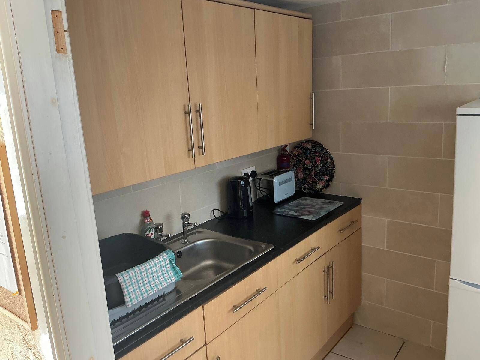 A small kitchen with wooden cabinets, a black countertop, a sink, a toaster, and a kettle.