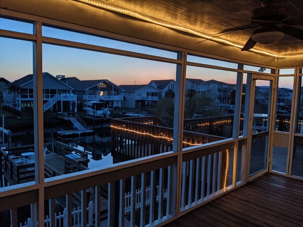 A view from a covered deck with wooden railings, overlooking a residential area with houses and a dock.