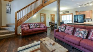 A spacious living area with a wooden staircase, two red sofas with patterned cushions, a dining area, and a kitchen with wooden cabinets and a refrigerator. - Coyote Cabin (Branson)