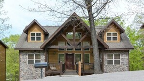 A two-story stone house with a wooden front porch, a central entrance, and a stone chimney. - Coyote Cabin (Branson)