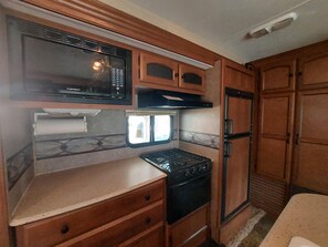 A compact RV kitchen with a microwave, stove, refrigerator, and wooden cabinetry. - Connie's Camp (Branson)