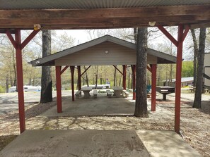 A covered picnic area with benches and picnic tables, surrounded by trees. - Connie's Camp (Branson)