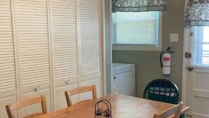 Uma área de refeições com mesa e cadeiras de madeira, um ventilador de teto, um relógio e uma janela com persianas.