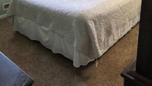 Quarto com cama, mesa de cabeceira, abajur e janela com persianas.