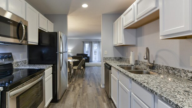 A modern kitchen with white cabinets, a granite countertop, stainless steel appliances, and a view to the dining area. - Glam R Us (Branson)