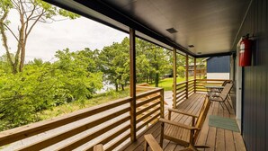 Une terrasse extérieure couverte, dotée de bancs et de tables en bois, qui offre une vue sur un paysage verdoyant et luxuriant ainsi que sur une étendue d’eau.
