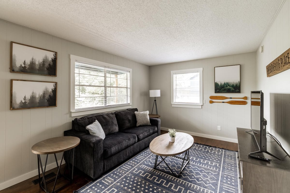 A living room with a dark gray sofa, two round coffee tables, a TV, and a patterned rug.