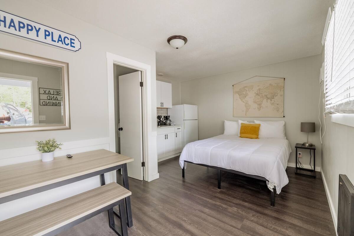 A hotel room with a bed, a desk, a map on the wall, and a kitchen area.