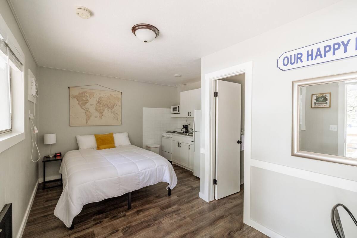 A bedroom with a bed, a world map on the wall, a kitchen area, and a sign saying "OUR HAPPY HOME".