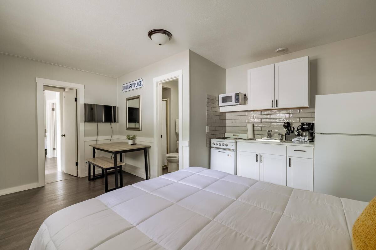 A hotel room with a bed, a desk, a microwave, a coffee maker, and a sign that says "OUR HAPPY PLACE".