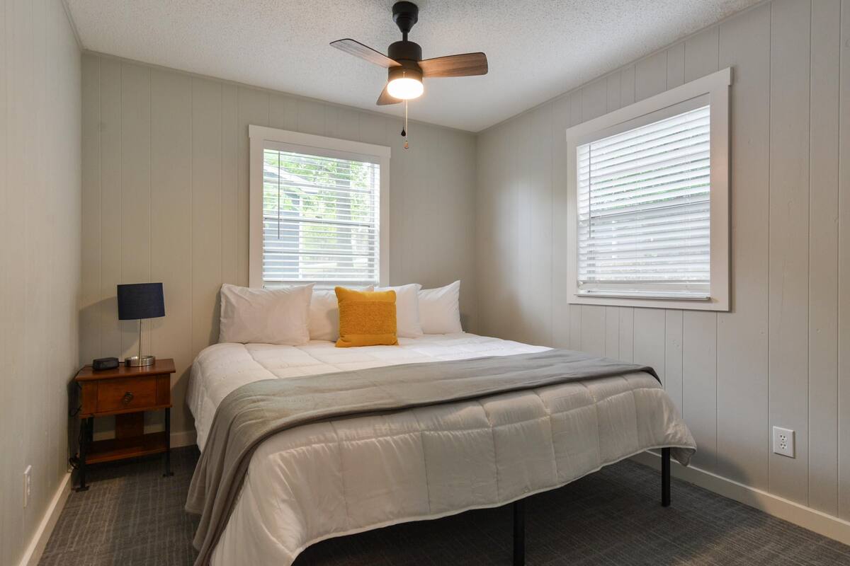 A bedroom with a bed, a nightstand, a ceiling fan, and two windows with blinds.