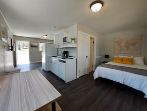 Quarto de hotel compacto com cozinha compacta, cama com almofadas amarelas, mapa na parede e mesa de madeira.