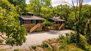 Deux cabanes dotées de terrasses et d’escaliers en bois, entourées d’une forêt dense et bordées d’un sentier de gravier.