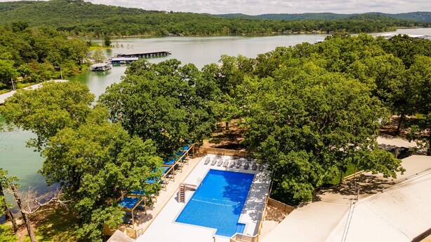 Une piscine entourée d’arbres luxuriants, avec un quai et des bateaux en arrière-plan.