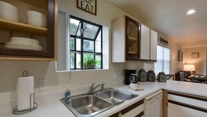 A modern kitchen with white countertops, stainless steel sinks, and wooden cabinets. - Farm Charm Condo (Branson)