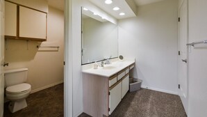 A bathroom with a toilet, sink, mirror, and cabinet. - Farm Charm Condo (Branson)