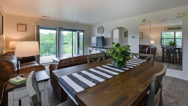 A modern living room with a wooden dining table, leather sofa, and a large window. - Farm Charm Condo (Branson)