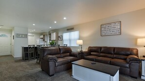 A living room with a brown leather sofa, a white coffee table, and a dining area with a kitchen in the background. - Farm Charm Condo (Branson)