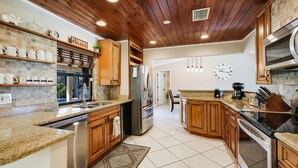 A kitchen with wooden cabinets, a stainless steel refrigerator, a microwave, and a dishwasher. - Incredible Lanai w/ Heated, Salt Pool, Extra-Wide Canal View, Southern Exposure! (Cape Coral)