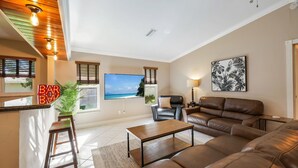 A living room with a brown leather sofa, a wooden coffee table, a TV on the wall, and a 'BAR' sign. - Incredible Lanai w/ Heated, Salt Pool, Extra-Wide Canal View, Southern Exposure! (Cape Coral)