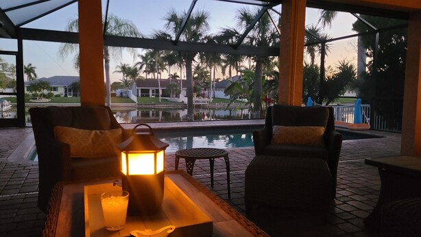 A poolside seating area with two chairs, a table, and a lantern. - Incredible Lanai w/ Heated, Salt Pool, Extra-Wide Canal View, Southern Exposure! (Cape Coral)