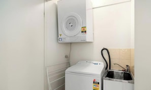 Un lavadero pequeño y compacto, con una secadora empotrada en la pared, un lavamanos y un panel de control.