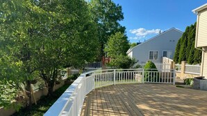 Eine Holzterrasse mit weißer Brüstung, umgeben von Bäumen und einem Haus im Hintergrund.