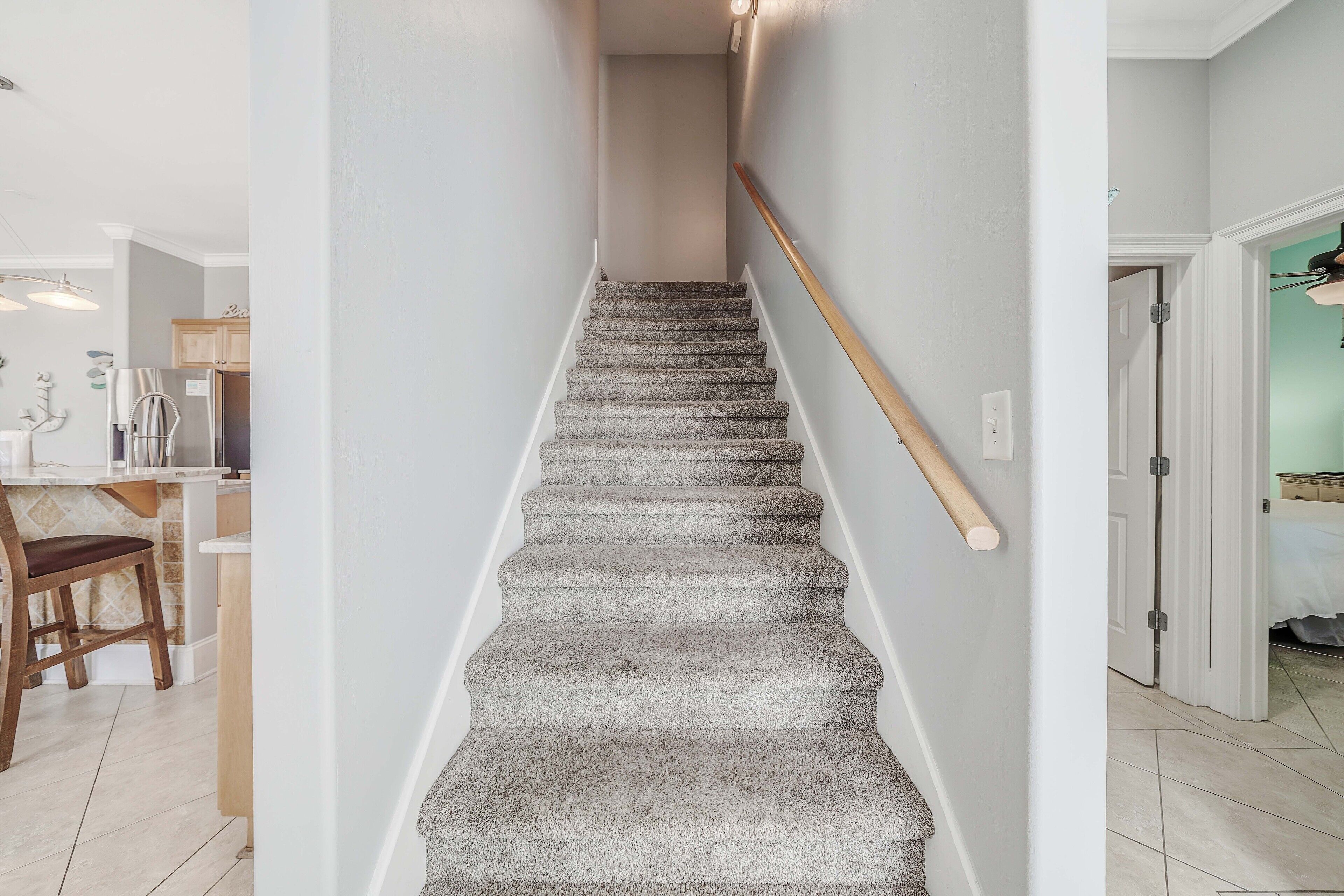 Un escalier avec une rampe en bois, des marches recouvertes de moquette et un interrupteur sur le mur.