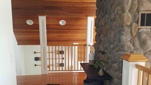 Una sala de estar con techo de madera, pared de piedra, alfombra de cuero de vaca y sofá de cuero azul con un cojín.