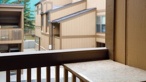 Un banc en bois avec une rambarde en métal, faisant partie d’un bâtiment aux murs extérieurs de couleur beige et doté d’un toit en pente.